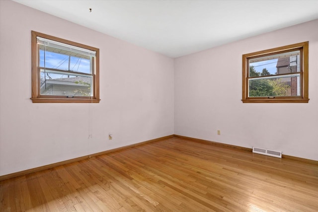 empty room featuring baseboards, visible vents, plenty of natural light, and light wood finished floors