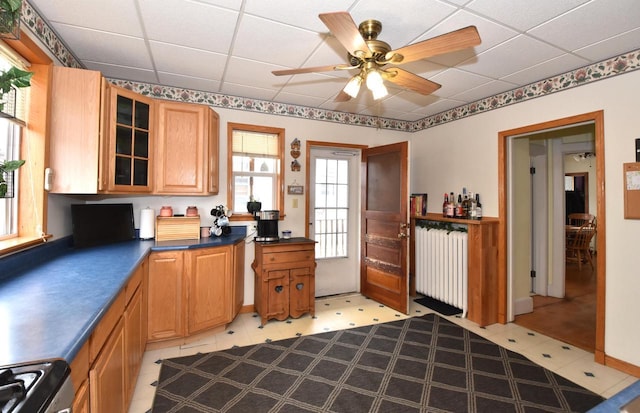 kitchen featuring glass insert cabinets, range with gas cooktop, dark countertops, radiator heating unit, and a drop ceiling