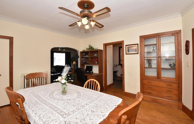 dining space with ceiling fan, crown molding, arched walkways, wood finished floors, and baseboards