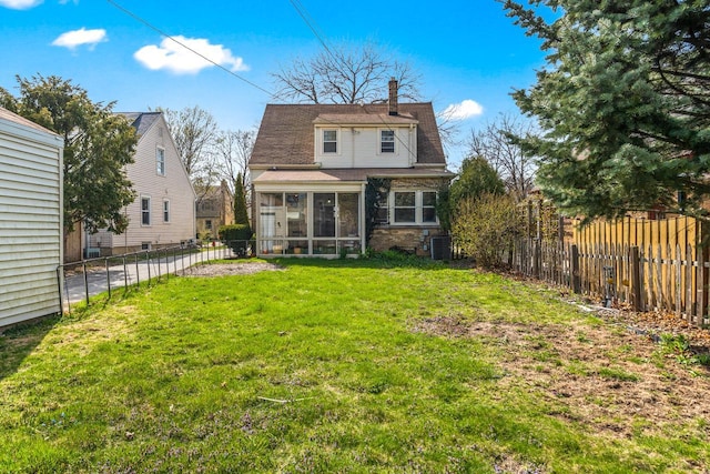 back of house featuring a chimney, a lawn, a sunroom, cooling unit, and a fenced backyard