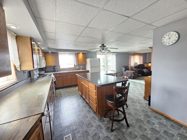 9878 Clark Dr, Marshfield, WI 54449 - kitchen featuring brown cabinetry, a kitchen island, white appliances, baseboards, and a ceiling fan