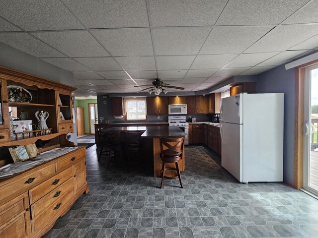 9878 Clark Dr, Marshfield, WI 54449 - kitchen featuring plenty of natural light, a kitchen bar, dark countertops, a drop ceiling, and white appliances