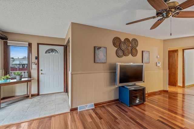 foyer with visible vents, wood finished floors, ceiling fan, a textured ceiling, and a wainscoted wall