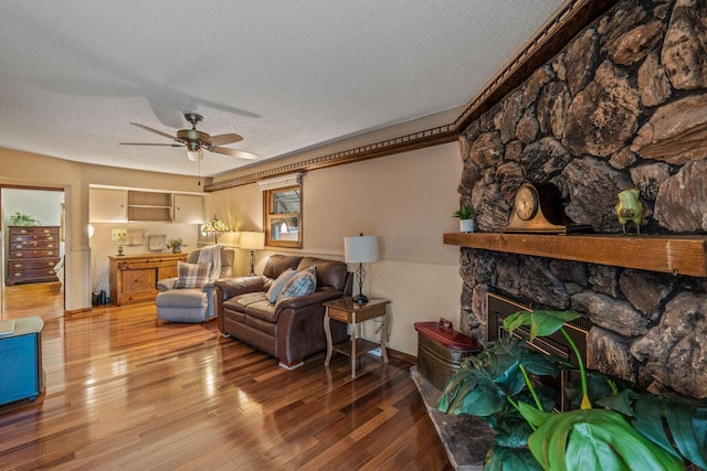 living room featuring ceiling fan, a fireplace, a textured ceiling, baseboards, and wood finished floors