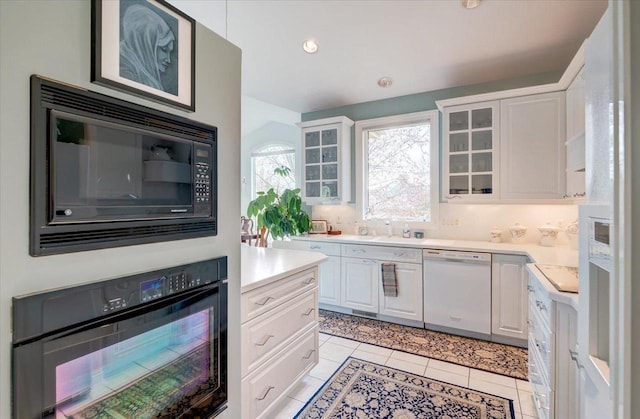 kitchen with light countertops, light tile patterned floors, black appliances, glass insert cabinets, and white cabinetry