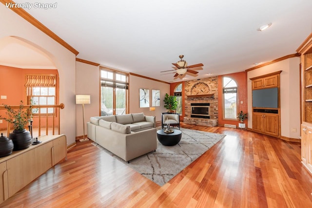 living room with ceiling fan, a fireplace, arched walkways, light wood-style flooring, and ornamental molding