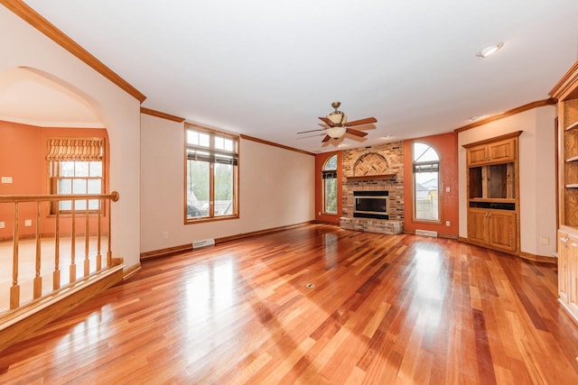unfurnished living room featuring visible vents, ornamental molding, a fireplace, ceiling fan, and light wood-type flooring