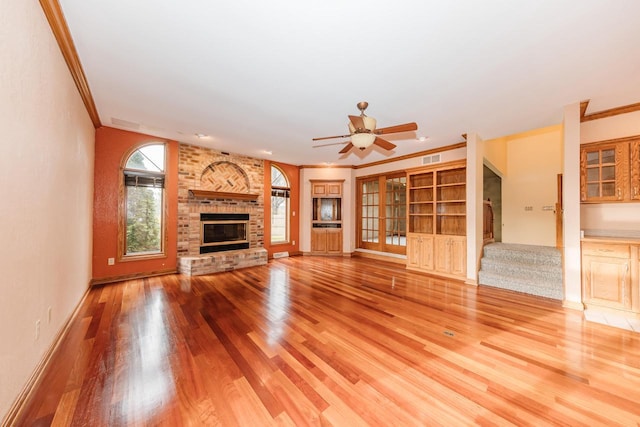 unfurnished living room featuring light wood-style floors, a ceiling fan, a brick fireplace, and crown molding
