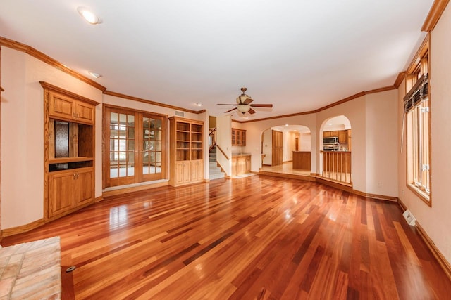 unfurnished living room featuring visible vents, baseboards, stairway, arched walkways, and light wood-style flooring