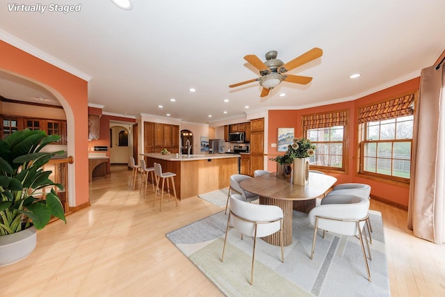 dining space featuring crown molding, arched walkways, light wood-style floors, and recessed lighting