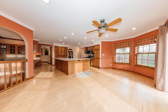 kitchen with crown molding, arched walkways, appliances with stainless steel finishes, and brown cabinets