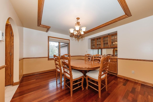 dining area with baseboards, arched walkways, wood finished floors, and a chandelier