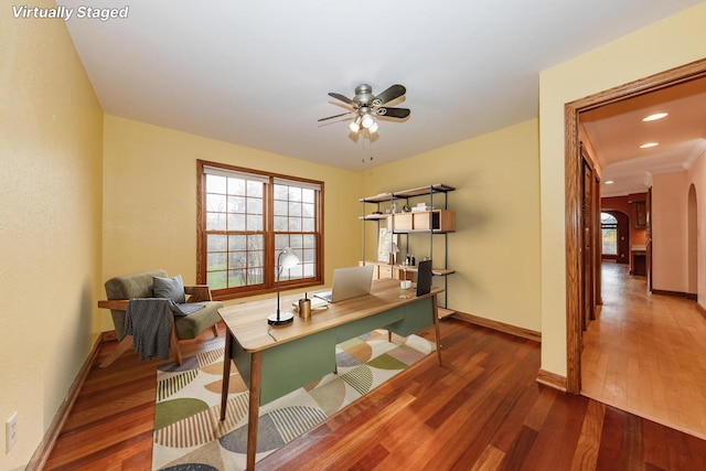 office area with arched walkways, ceiling fan, wood finished floors, and a wealth of natural light