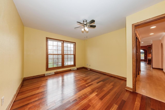 empty room with ceiling fan, visible vents, arched walkways, wood finished floors, and baseboards