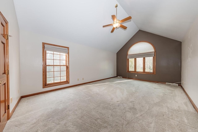 empty room with baseboards, a ceiling fan, vaulted ceiling, and light colored carpet