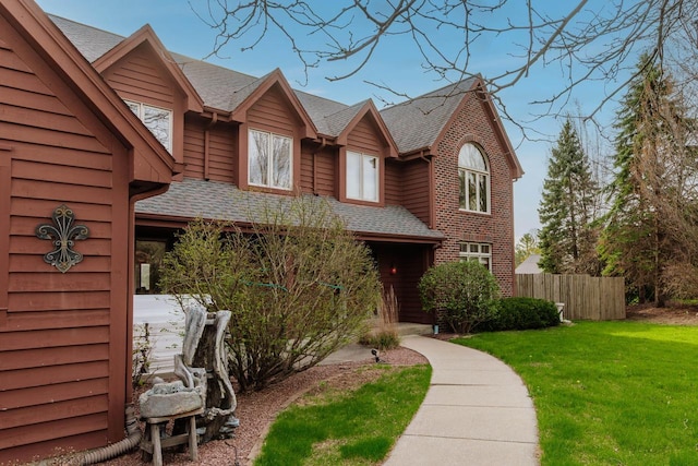 view of front of house featuring roof with shingles, fence, and a front lawn
