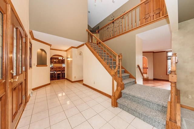stairs with tile patterned flooring, crown molding, a towering ceiling, baseboards, and arched walkways