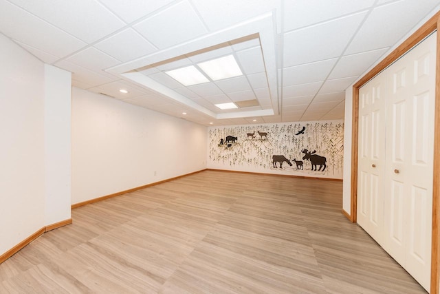 basement featuring baseboards, a paneled ceiling, and light wood finished floors
