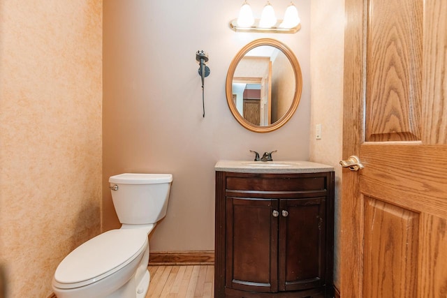 half bathroom featuring vanity, baseboards, wood finished floors, and toilet