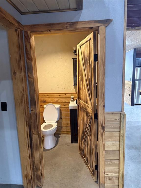 8523 Lakeside Rd, Trego, WI 54888 - bathroom featuring wooden walls, concrete flooring, a sink, toilet, and a wainscoted wall