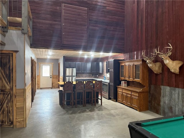 8523 Lakeside Rd, Trego, WI 54888 - interior space featuring a kitchen breakfast bar, wood walls, a center island, stainless steel appliances, and finished concrete floors
