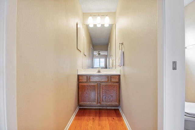 bathroom featuring baseboards, wood finished floors, toilet, and vanity