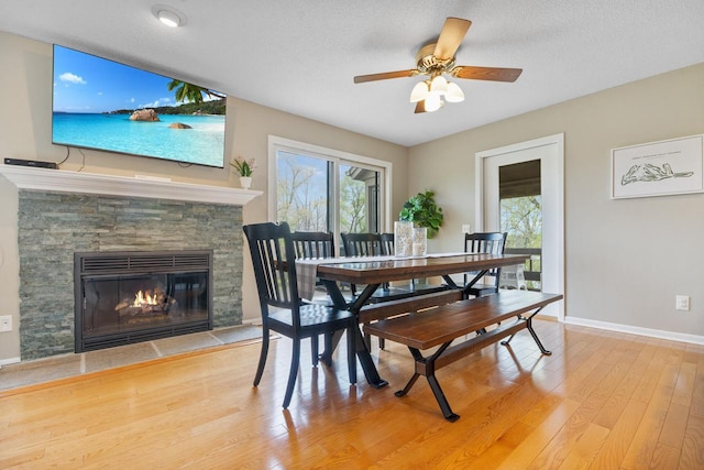 dining area with a ceiling fan, baseboards, wood finished floors, and a fireplace