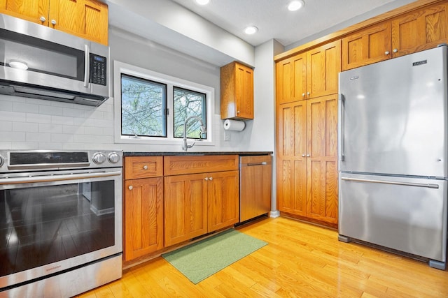kitchen with brown cabinets, appliances with stainless steel finishes, decorative backsplash, and light wood-type flooring