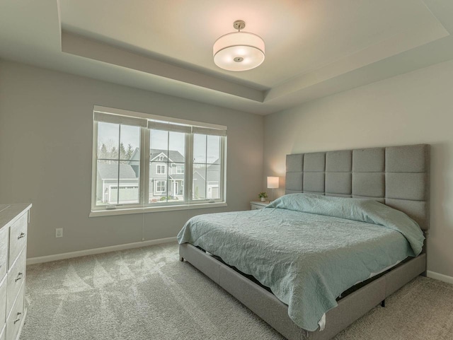 bedroom with a tray ceiling, light colored carpet, and baseboards