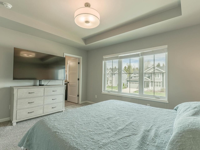 bedroom featuring a tray ceiling, light colored carpet, and baseboards
