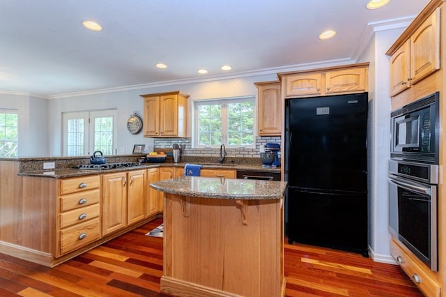 kitchen featuring plenty of natural light, a peninsula, wood finished floors, and black appliances