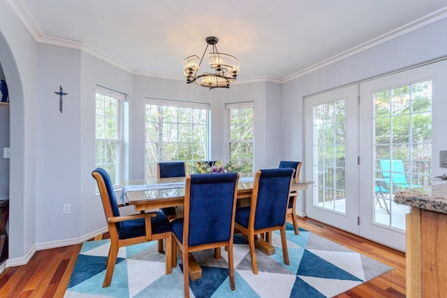 dining space with an inviting chandelier, arched walkways, baseboards, wood finished floors, and ornamental molding