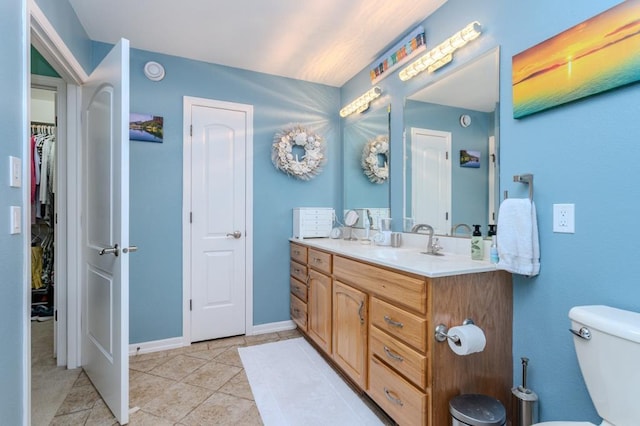 bathroom featuring a walk in closet, tile patterned flooring, vanity, toilet, and baseboards