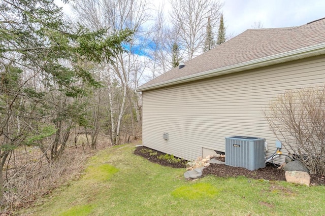 view of home's exterior with a lawn, central AC unit, and a shingled roof