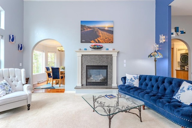 carpeted living area featuring arched walkways, stacked washer and dryer, a glass covered fireplace, and a high ceiling