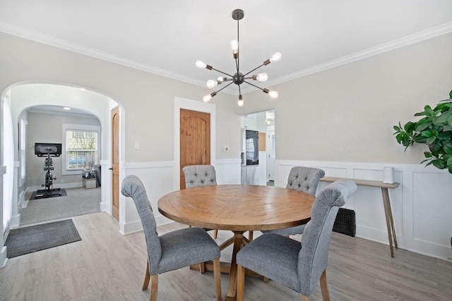 dining area featuring light wood-style floors, arched walkways, a chandelier, and ornamental molding