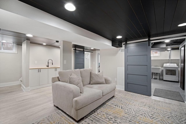 living room with baseboards, a barn door, washer / dryer, and light wood finished floors