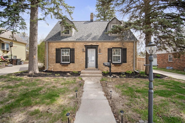 new england style home featuring fence, a shingled roof, a chimney, and brick siding
