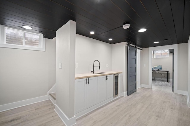bar featuring a barn door, a sink, baseboards, beverage cooler, and light wood-style floors