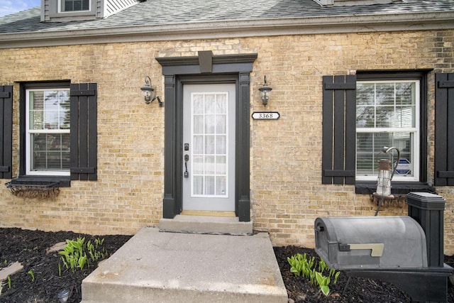 property entrance with a shingled roof and brick siding