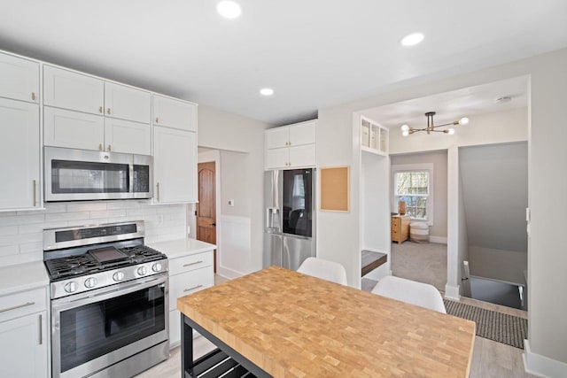 kitchen with white cabinets, a notable chandelier, appliances with stainless steel finishes, light countertops, and decorative backsplash