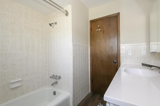 bathroom featuring tile walls, wood finished floors, a wainscoted wall, vanity, and tub / shower combination