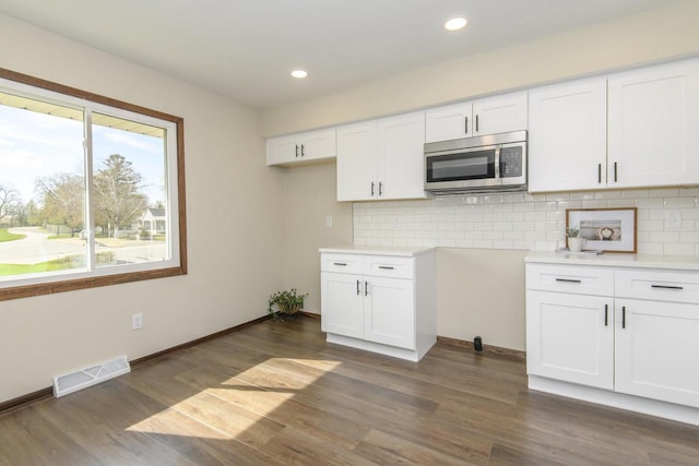 kitchen with white cabinetry, stainless steel microwave, backsplash, visible vents, and dark wood-style floors