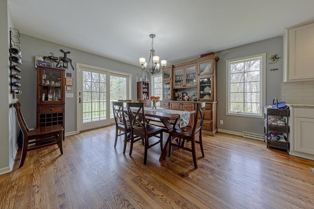 dining space with visible vents, light wood-style flooring, baseboards, and a notable chandelier