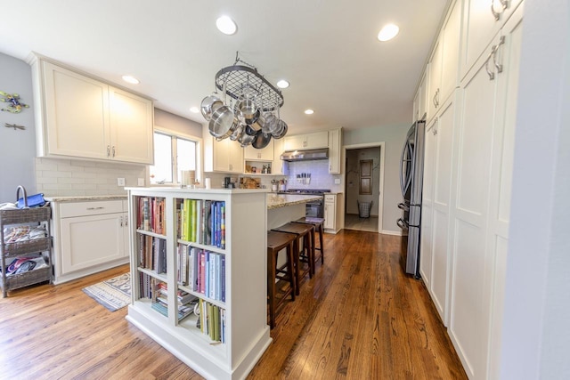 kitchen with appliances with stainless steel finishes, backsplash, a kitchen bar, under cabinet range hood, and a kitchen island