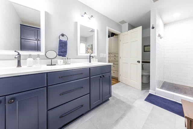 bathroom with double vanity, toilet, a tile shower, and a sink