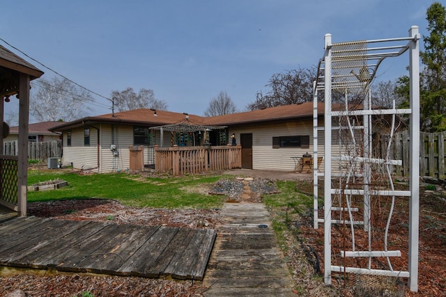 rear view of property featuring a lawn, fence, a wooden deck, and central AC unit