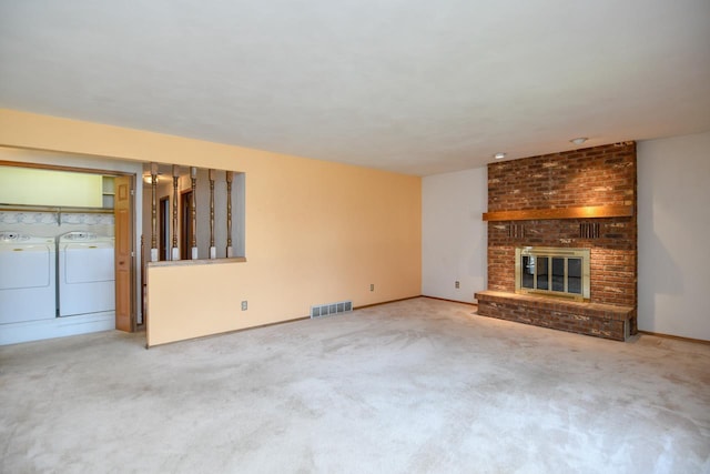 unfurnished living room featuring carpet flooring, a brick fireplace, separate washer and dryer, baseboards, and visible vents
