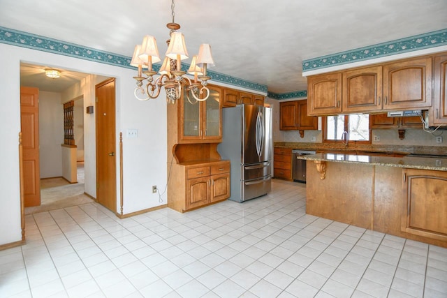 kitchen with light stone countertops, brown cabinets, baseboards, a chandelier, and stainless steel appliances