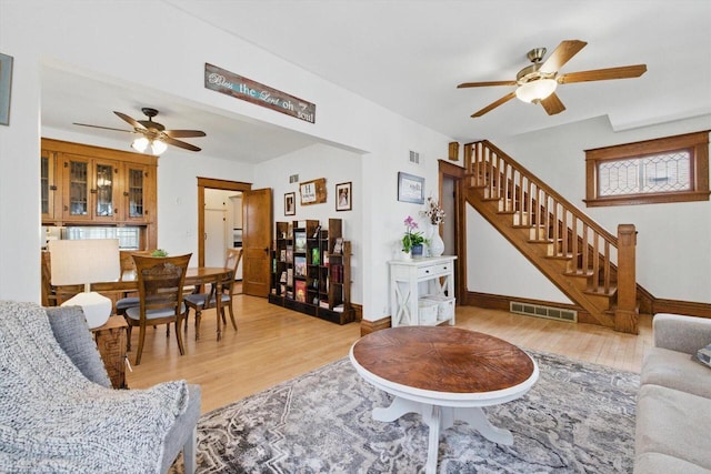living room featuring ceiling fan, visible vents, light wood-style flooring, and stairway
